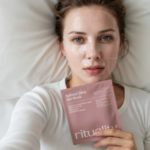 Woman lying down holding Rituality Salmon DNA Collagen Mask with relaxed expression and minimal background